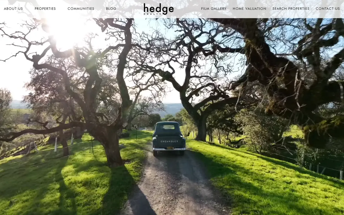 Hedge Realty home page: the hedge wordmark centred in a white menu bar with About us, Properties, Communities and Blog on the left and Film gallery, Home valuation, Search properties and Contact us on the right, over a full-width video still of an old pickup truck on a dirt road under oak trees
